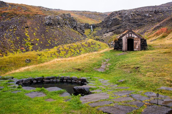 Guðrúnarlaug natural baths with a tiny wooden house behind in Iceland