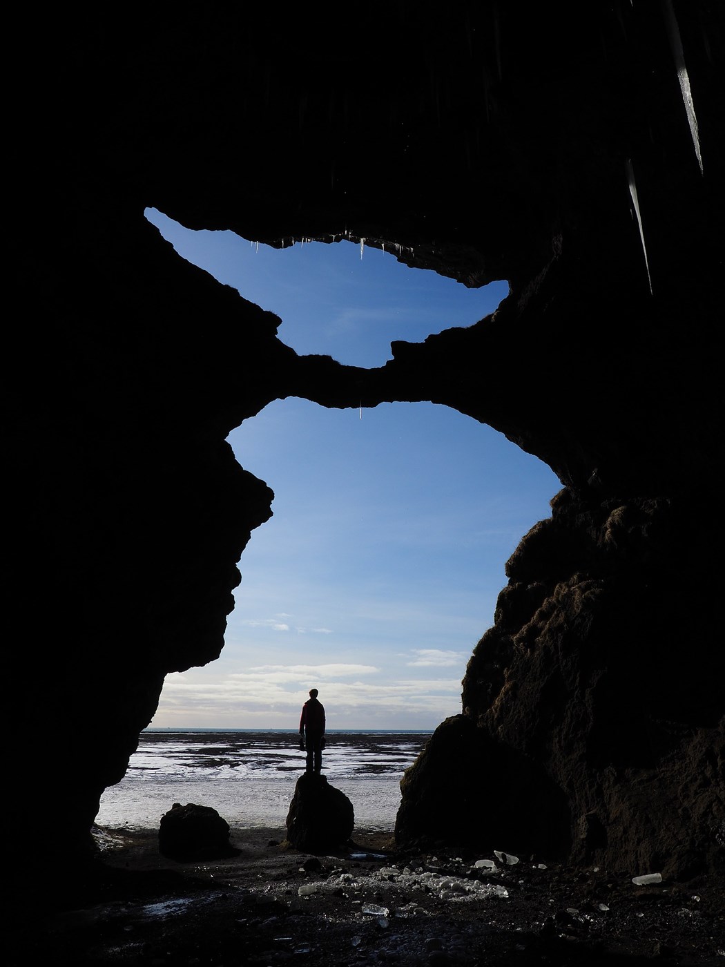 Hjorleifshofdi cave in Iceland, a man standing in front of the cave, blue sky