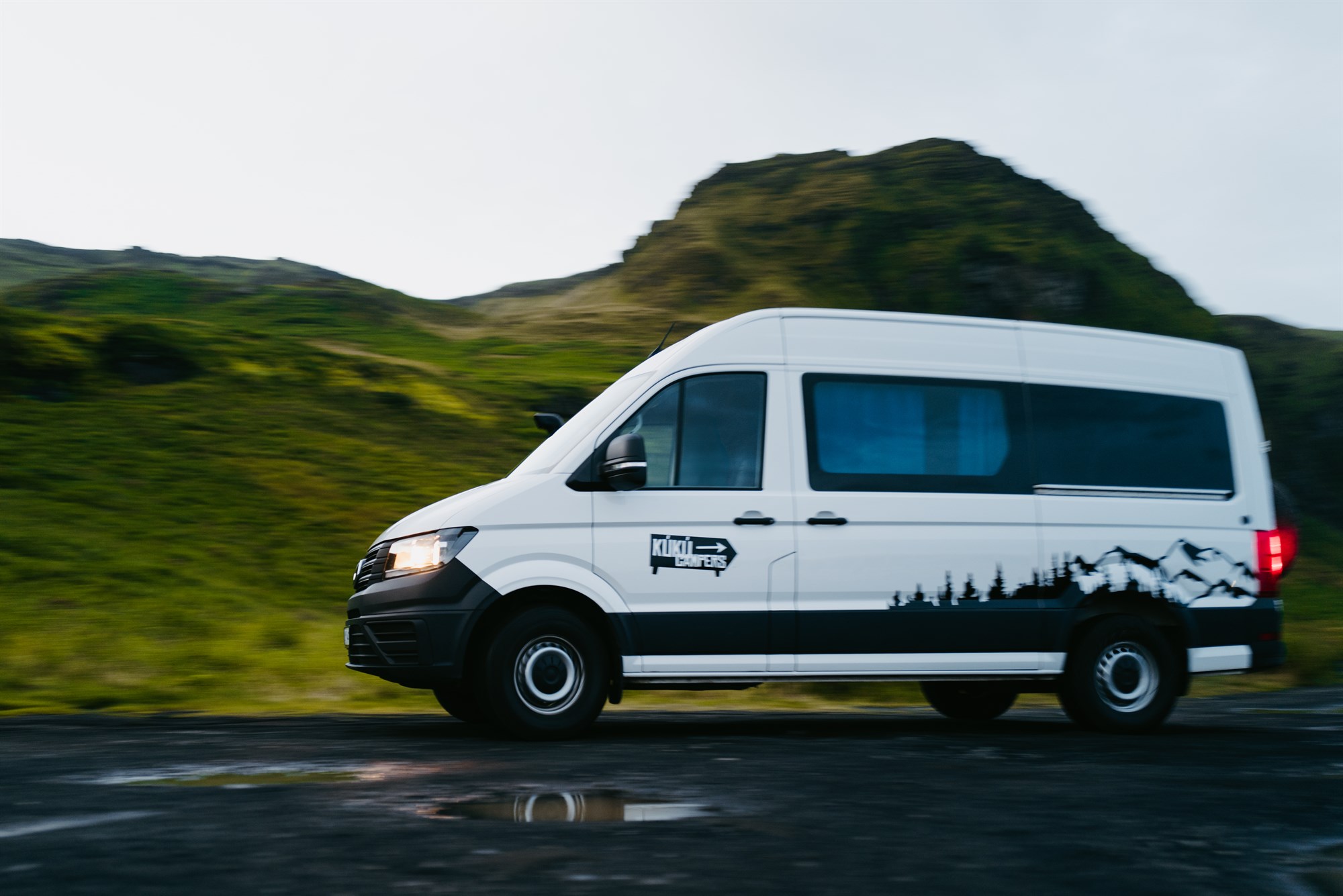Van aménagé KuKu Campers roulant sur une route en Islande entouré de paysages naturels, expérience de road trip en Islande entre liberté et immersion