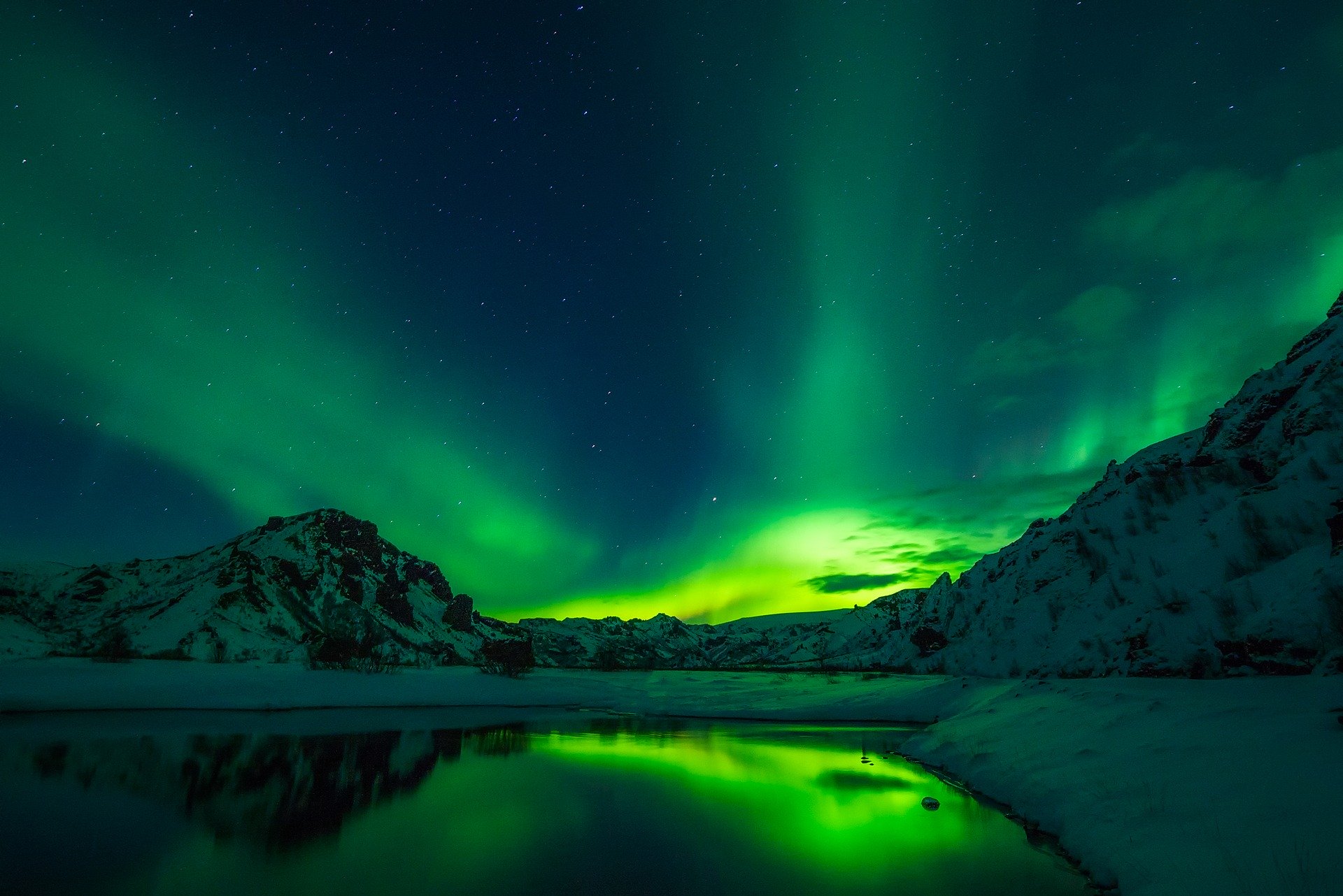 Green northern lights in iceland at night, lake one the foreground, mountains on the background