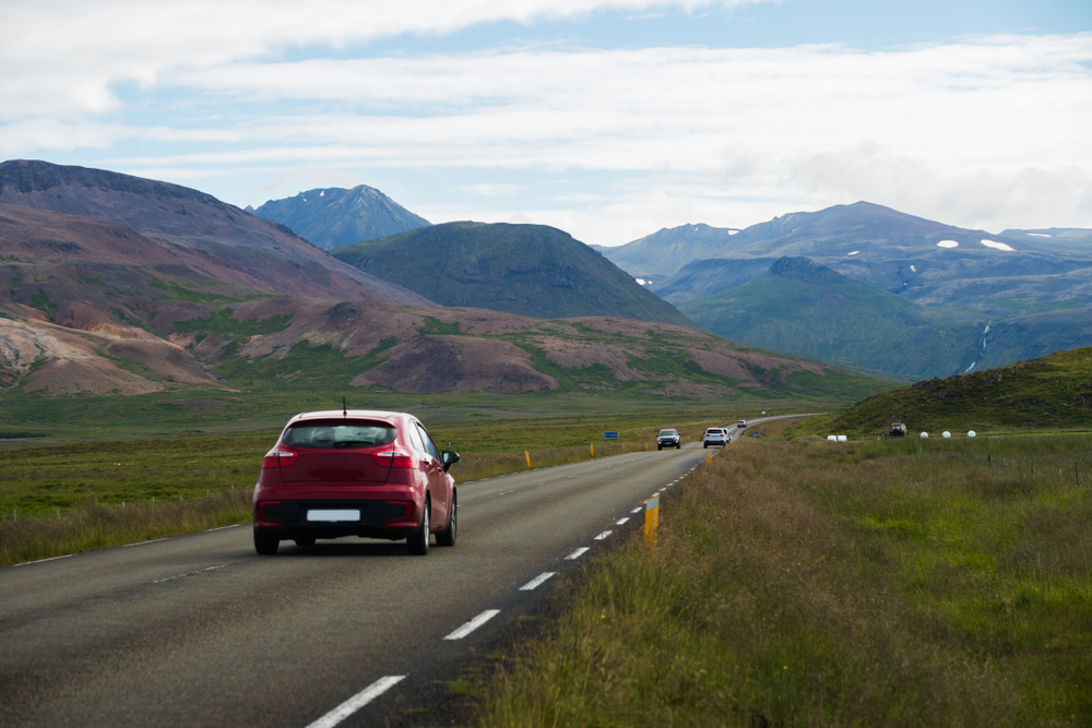 Voiture roulant sur une route islandaise entourée de montagnes, scène typique d’un road trip en Islande.