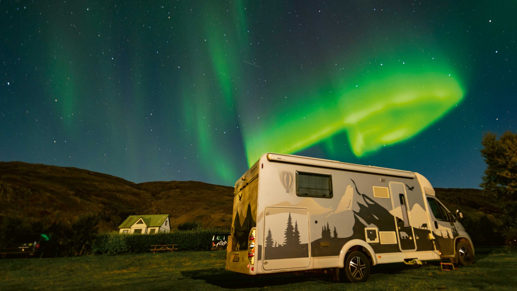 Camping-car stationné sous les aurores boréales en Islande, expérience unique de road trip nocturne.