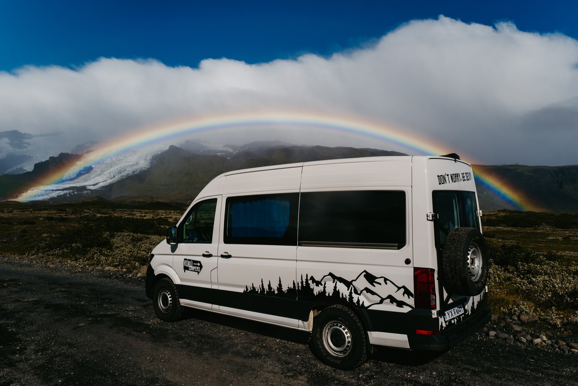 Campervan sous un arc-en-ciel en Islande, symbole des conditions météo changeantes et de la beauté du road trip.